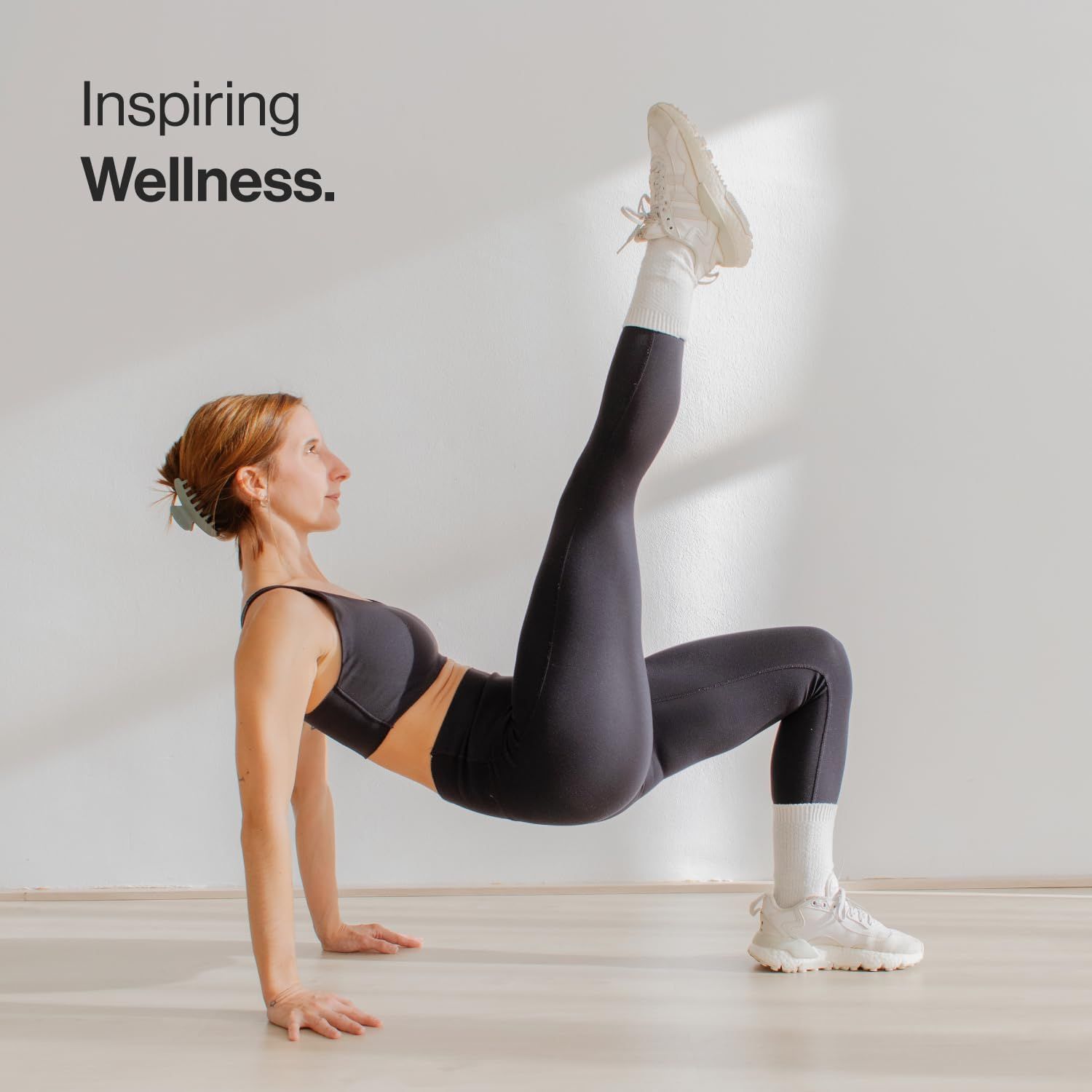Donna in abbigliamento sportivo, gamba in aria. Sfondo: bianco. Testo: Inspiring Wellness.
