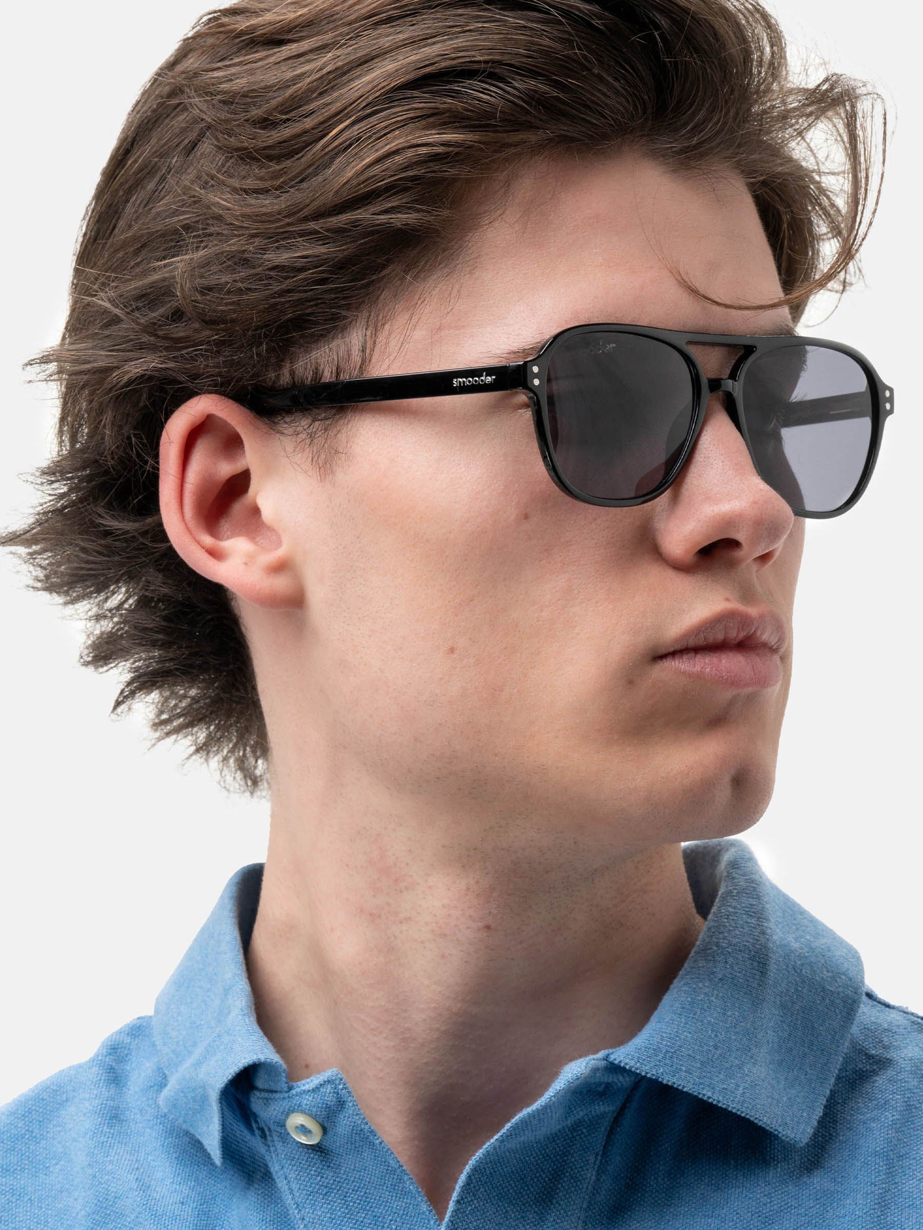 Uomo con occhiali da sole neri con lenti scure. Montatura lucida. Marchio sull'asta.