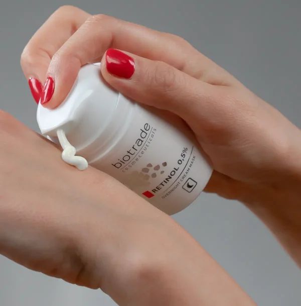 Flacone bianco con scritta Biotrade, Retinolo 0,5%. Crema applicata sulla mano. Maschera notte.