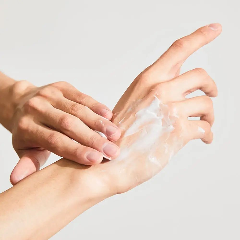 Mani, una strofinata con crema. La crema è bianca. Pelle chiara. Lo sfondo è chiaro.