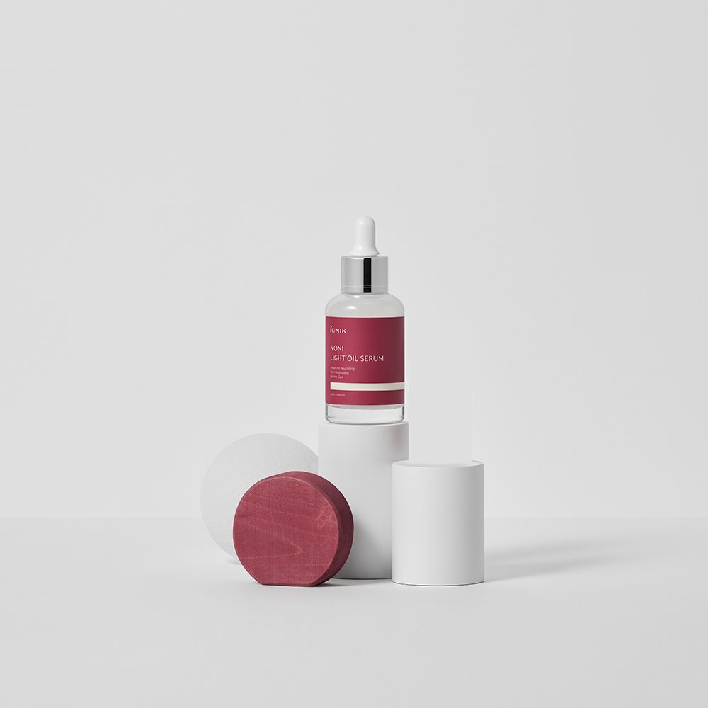 Flacone di siero con etichetta rossa su piedistallo bianco. Oggetto rotondo rosso accanto. Contagocce. Contenitore trasparente.