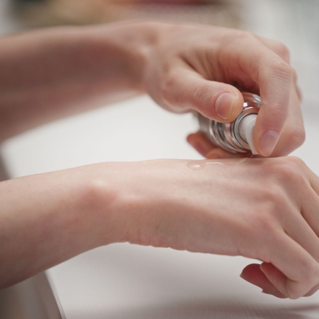 Mani che applicano il siero sulla pelle. Il flacone non è visibile.