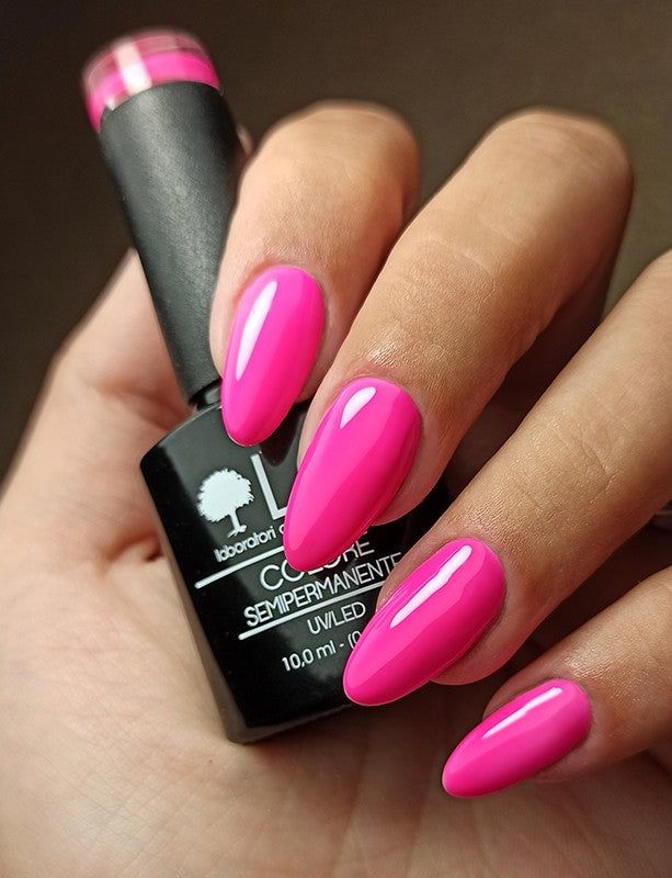 Mano con unghie smaltate e flacone di smalto. Unghie rosa, flacone nero con scritta.