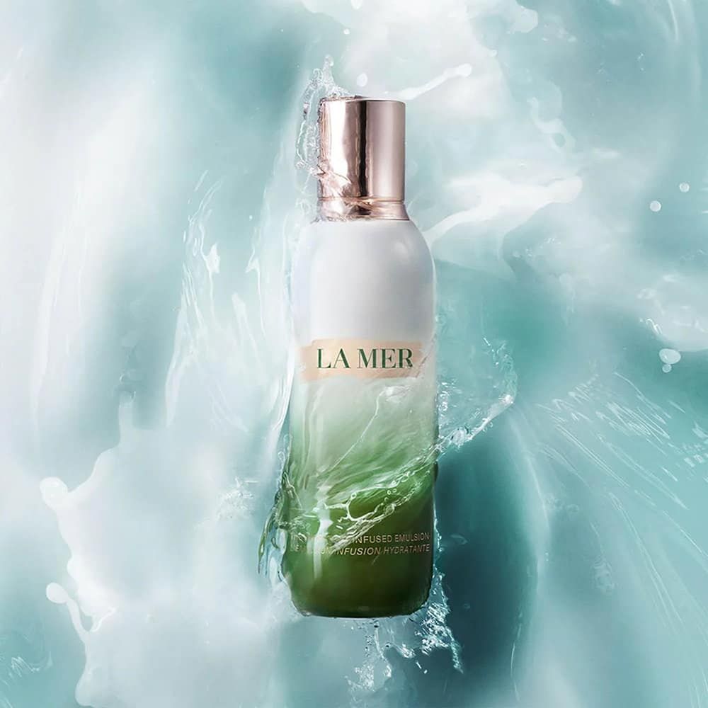 Flacone bianco e verde con tappo dorato. Scritta "LA MER". L'acqua schizza intorno al flacone.