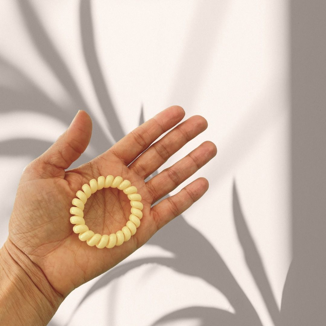 Palmo della mano con un elastico a spirale giallo. Sfondo con ombre.