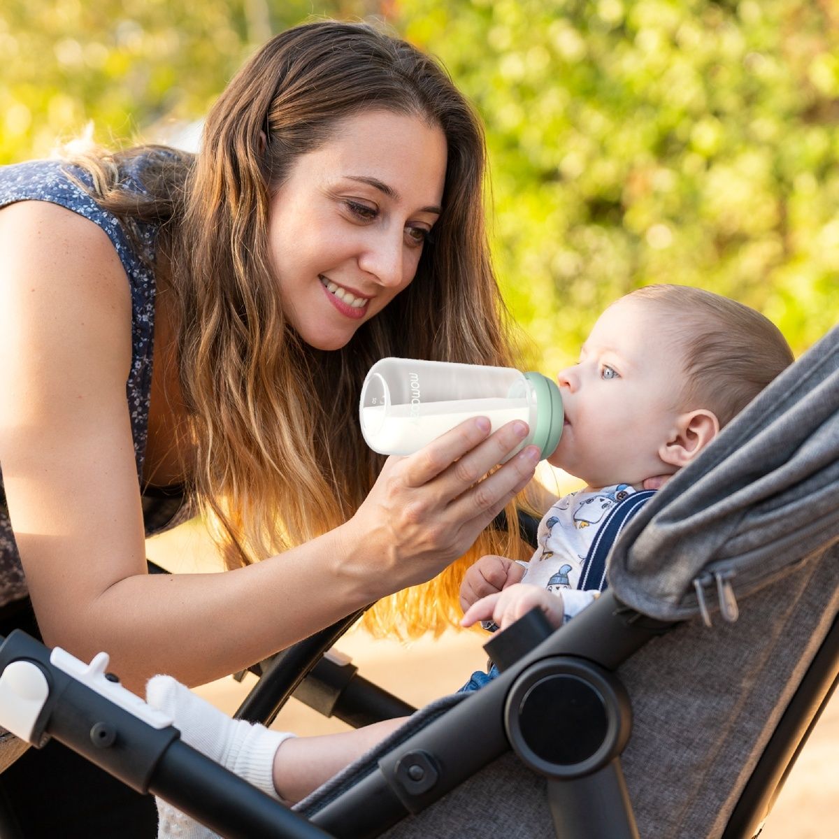 Donna che allatta il bambino in carrozzina con biberon. Il bambino beve dal biberon.