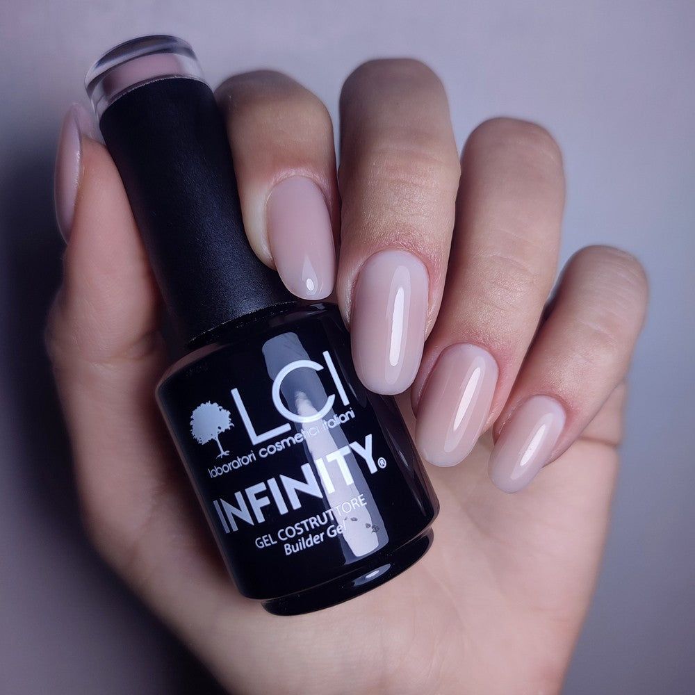 Mano con unghie smaltate. Flacone di gel costruttore LCI Cosmetics Infinity. Gel rosa chiaro applicato sulle unghie.