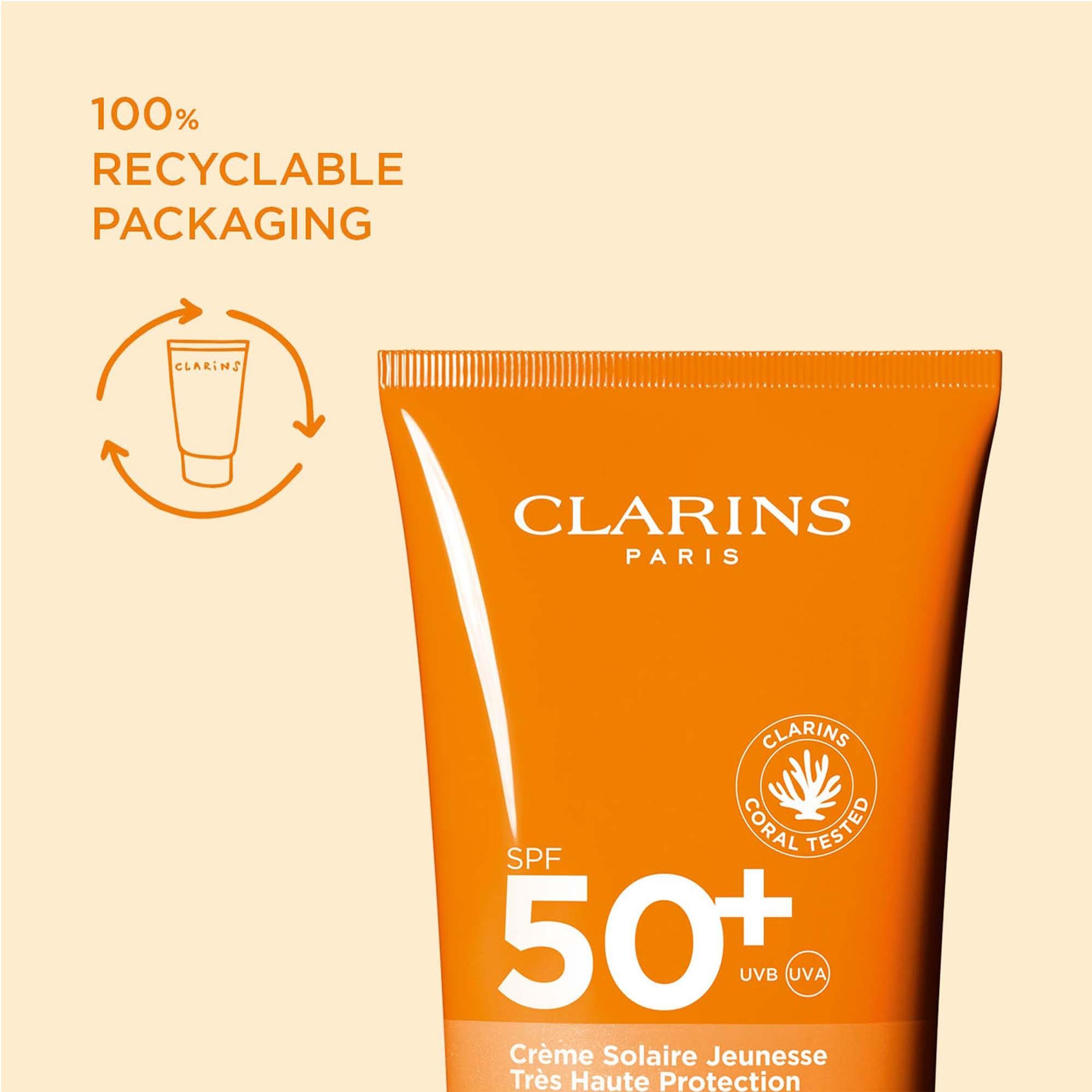 Tubo arancione di crema solare. Testo: Imballaggio riciclabile al 100%. Logo Clarins Paris. SPF 50+. Testato corallo.