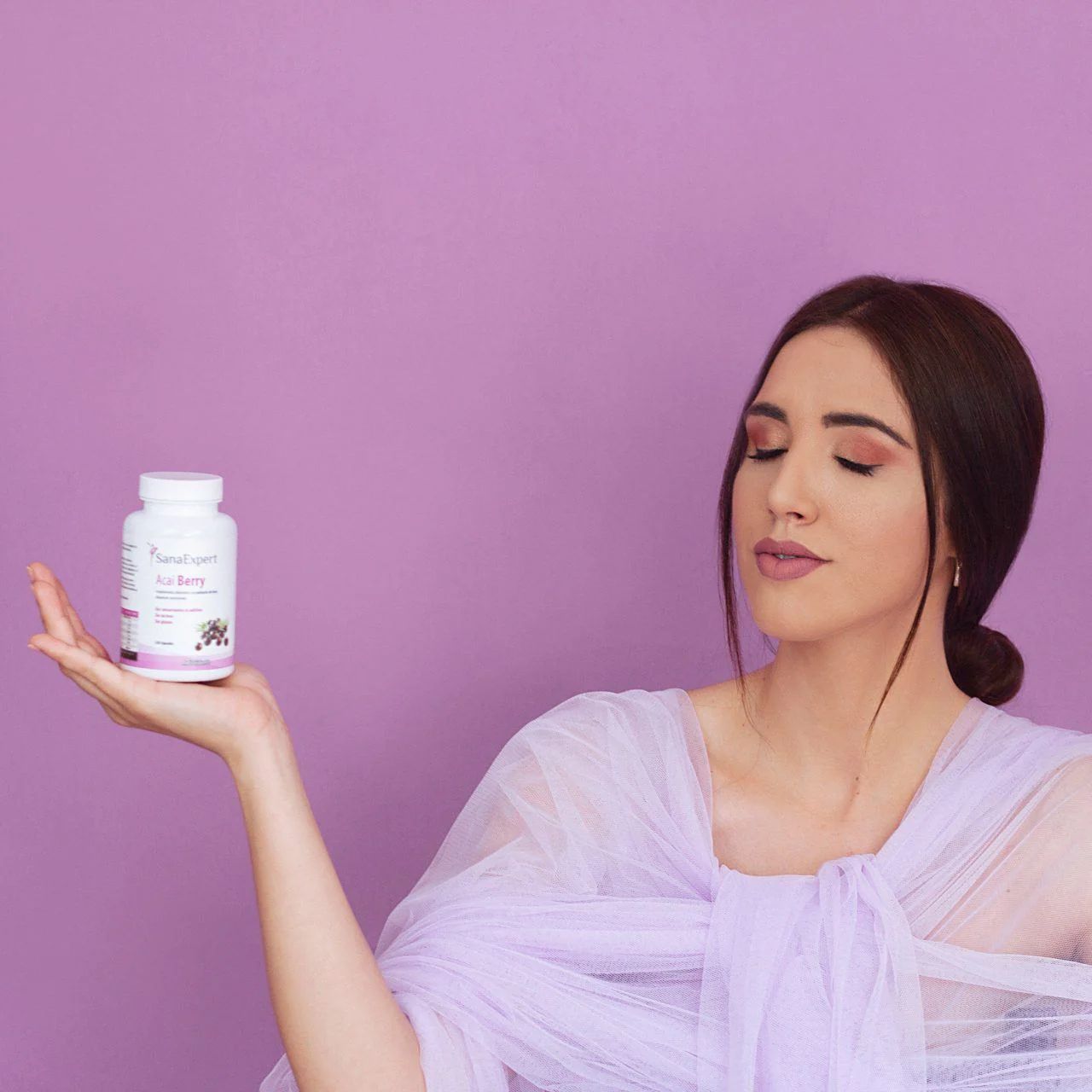 Una donna tiene una bottiglia di Acai Berry. L'etichetta del prodotto è visibile. La donna indossa un abito viola.