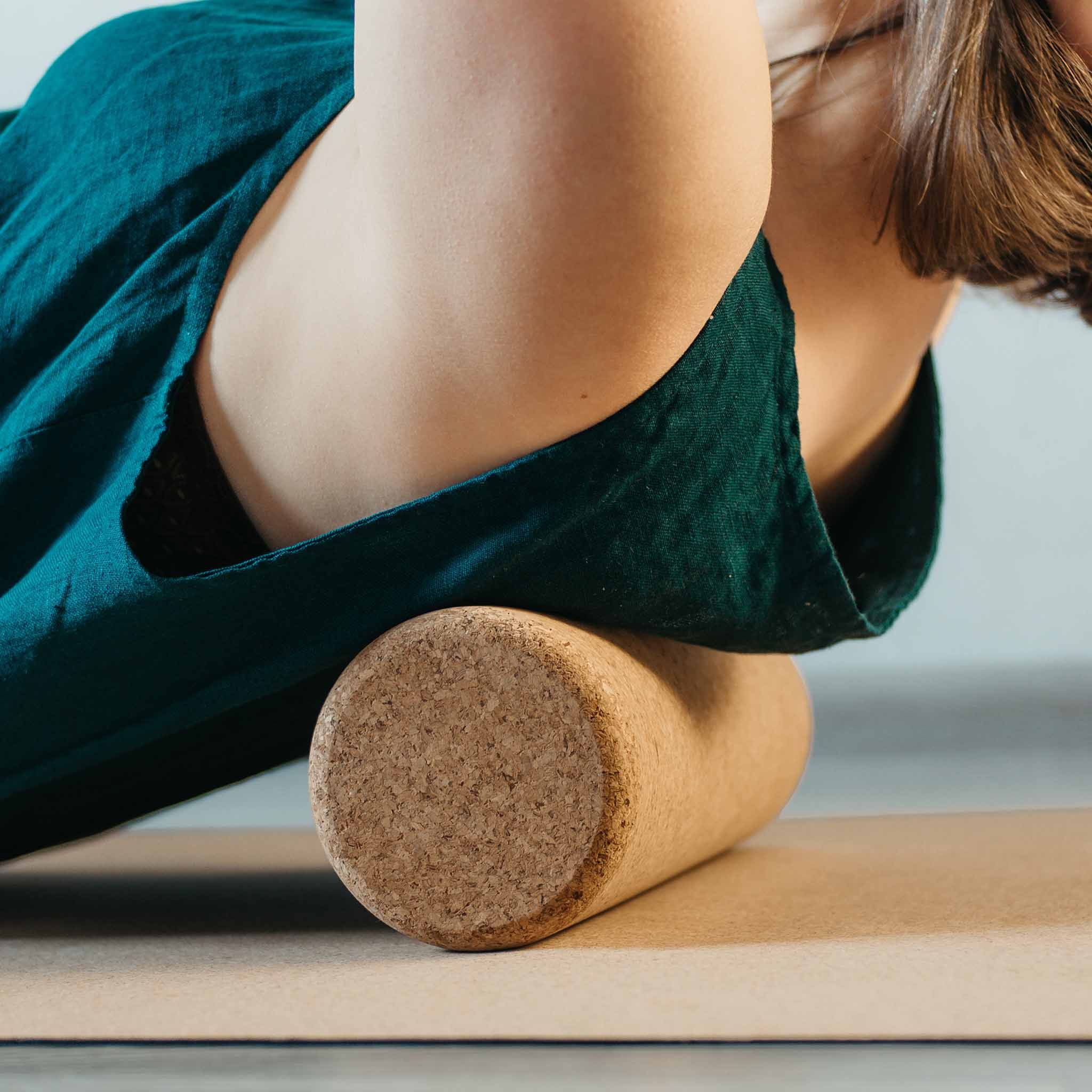 Persona che usa un rullo per fascia in sughero. Rullo marrone sotto la schiena su un tappetino.