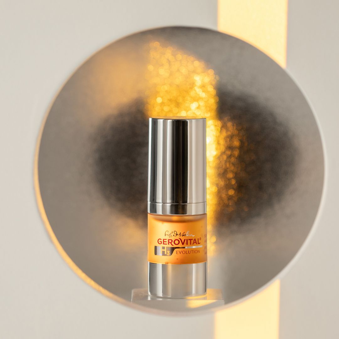 Flacone di siero davanti a uno specchio rotondo. Corpo argentato, contenuto giallo. Scritta: Gerovital Evolution.