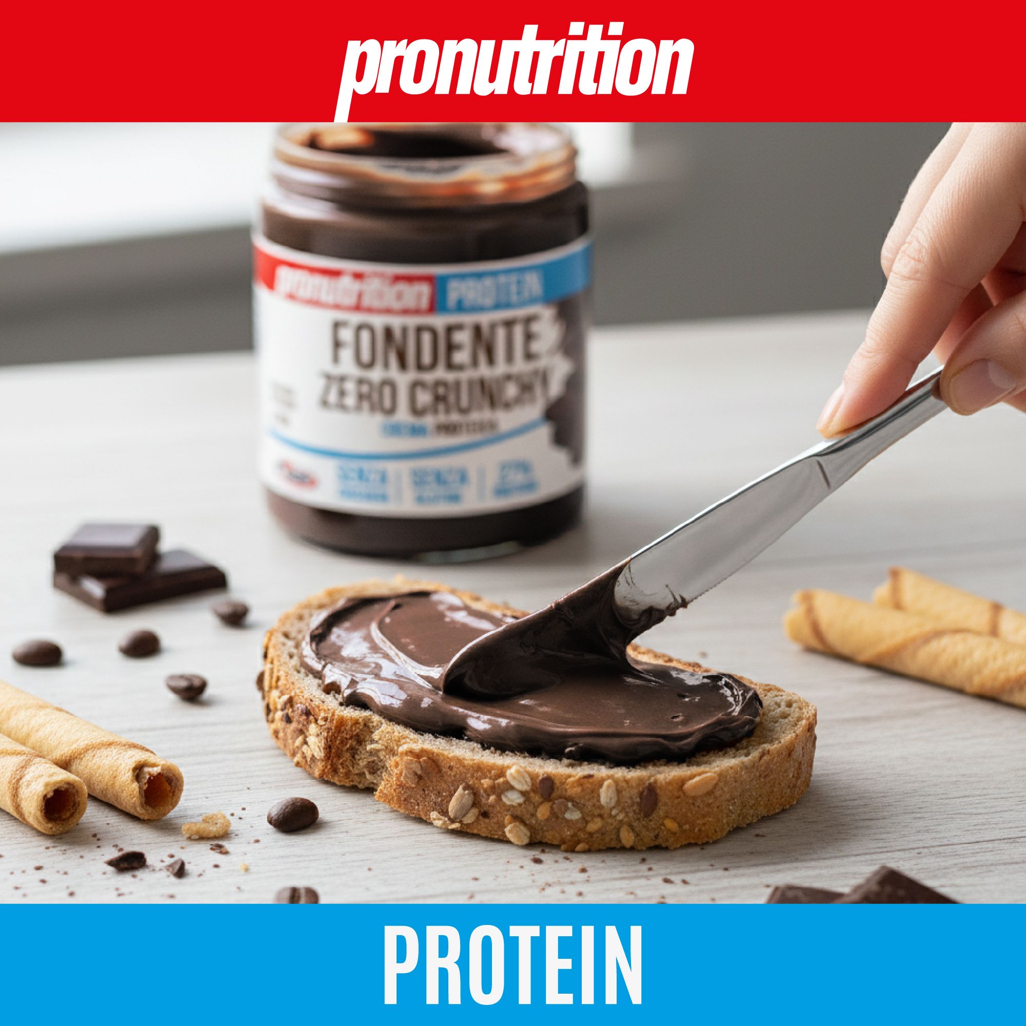 Crema scura spalmata sul pane. Scritta: Fondente Zero Crunchy, Crema Proteica. Testo: Senza zucchero, glutine, 27% proteine. Una mano tiene un coltello.