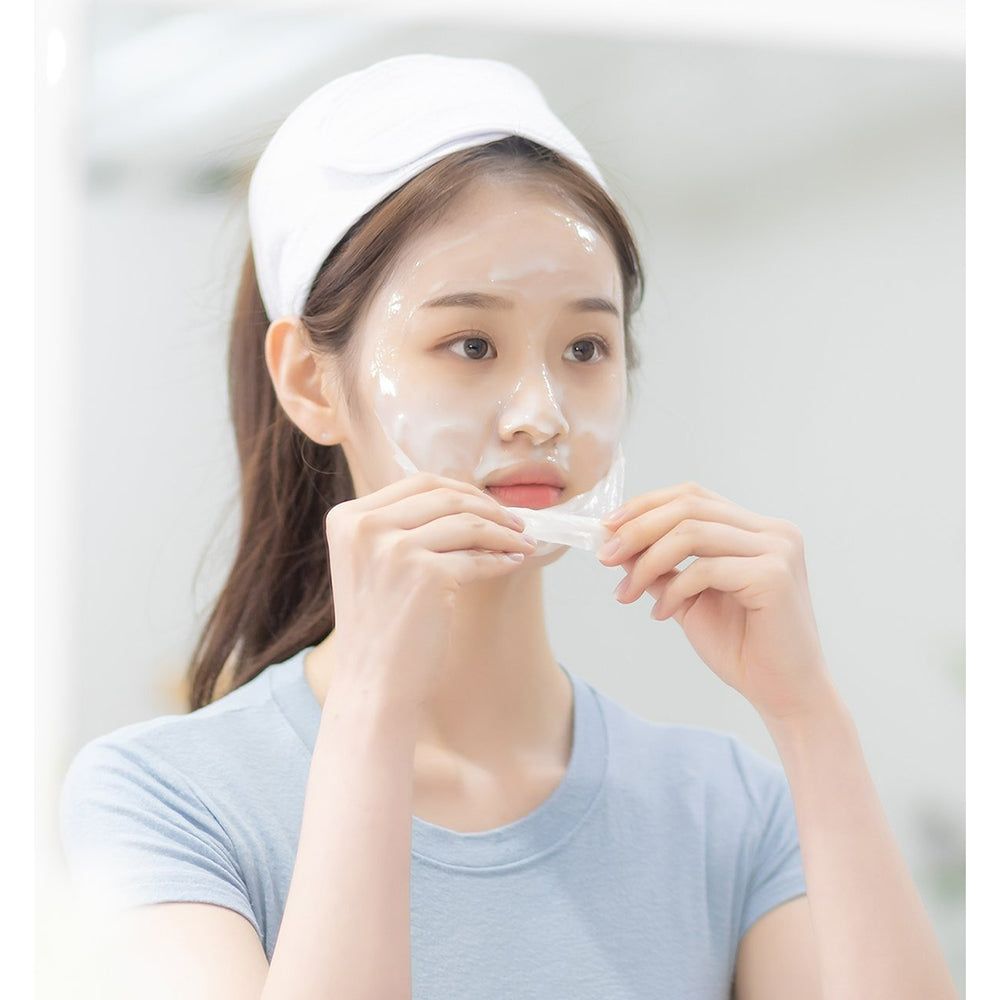 Donna con maschera viso, che rimuove un foglio trasparente. Indossa una fascia.