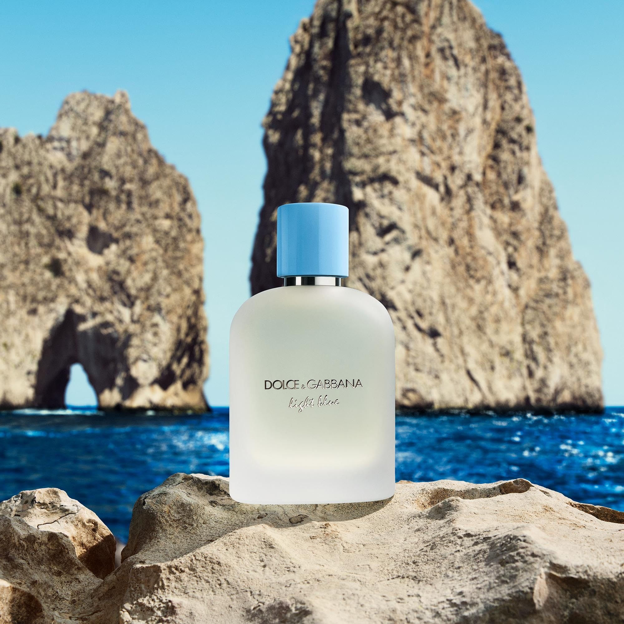 Flacone di profumo su una roccia davanti a un paesaggio marino. Scritta: Dolce & Gabbana Light Blue. Tappo azzurro chiaro.