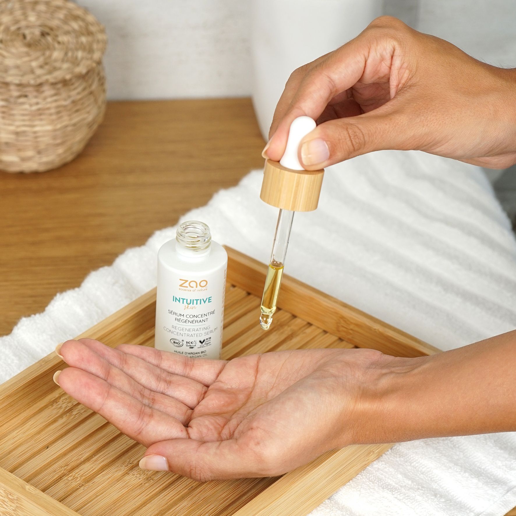 Flacone bianco con pipetta. Goccia di siero sulla mano. Scritta: ZAO, Intuitive, Sérum concentré régénérant. Su vassoio di legno.