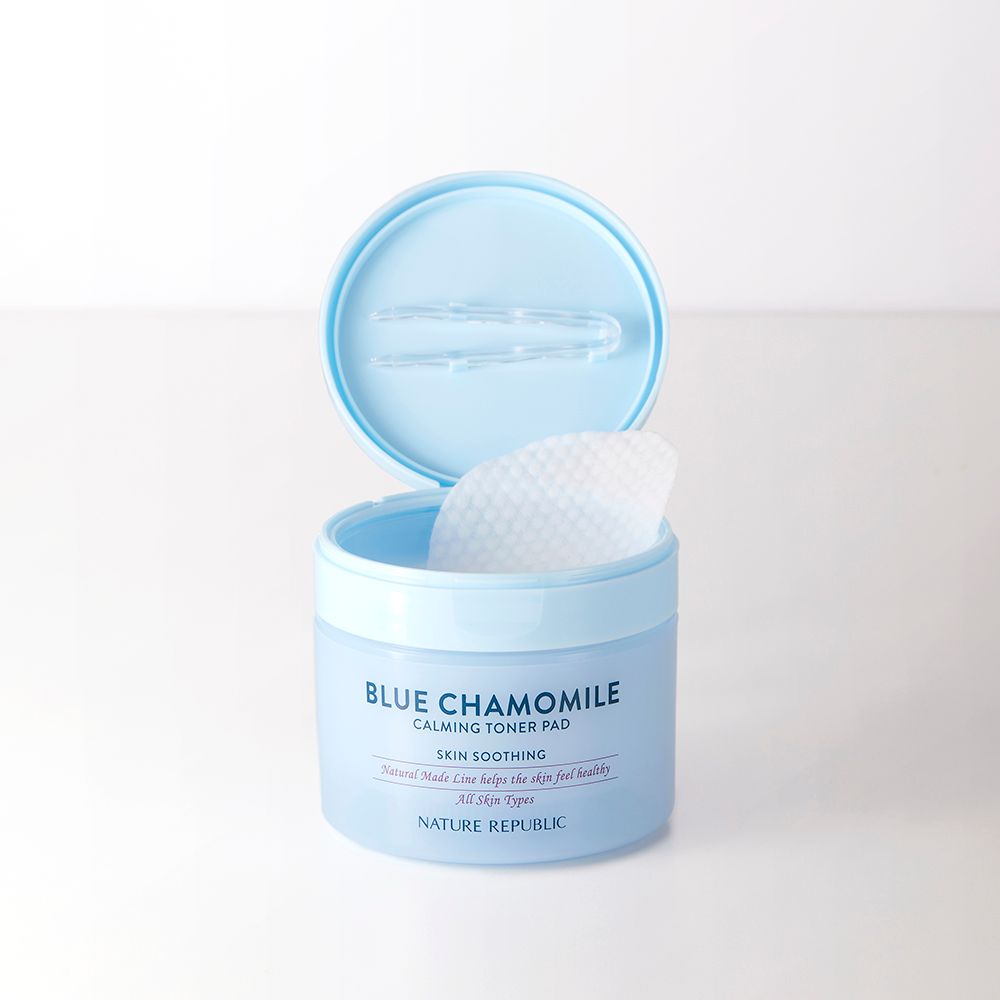 Barattolo azzurro con coperchio aperto. Contiene dischetti tonici bianchi. Scritta: Blue Chamomile, Calming Toner Pad, Nature Republic.