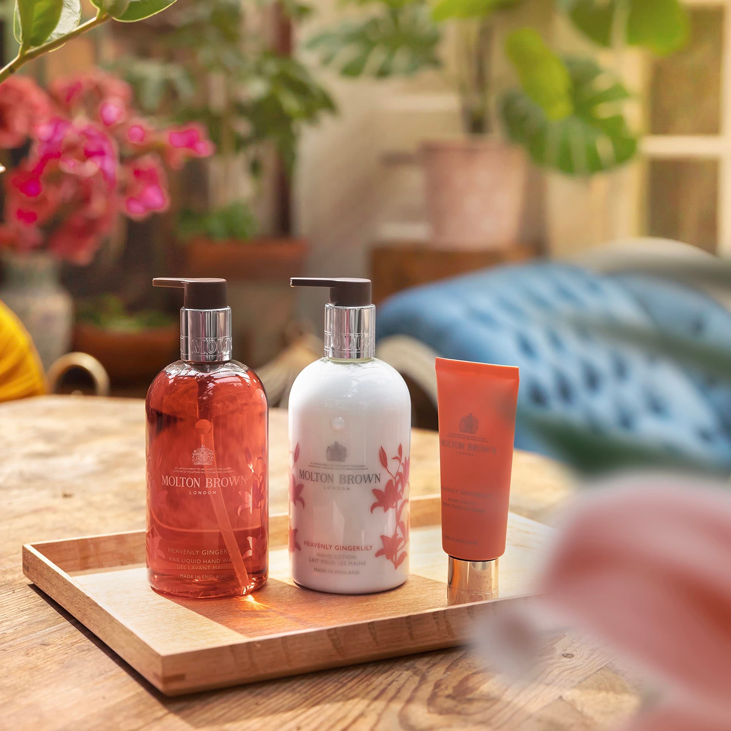 Vassoio in legno con tre prodotti: saponi liquidi rosso e bianco, e un tubetto. Scritta: Molton Brown. Piante sullo sfondo.