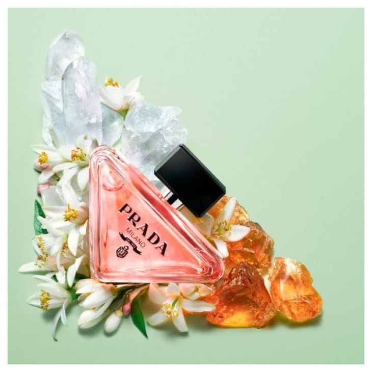 Flacone di profumo rosa, circondato da fiori e cristalli. Tappo nero. Scritta PRADA.