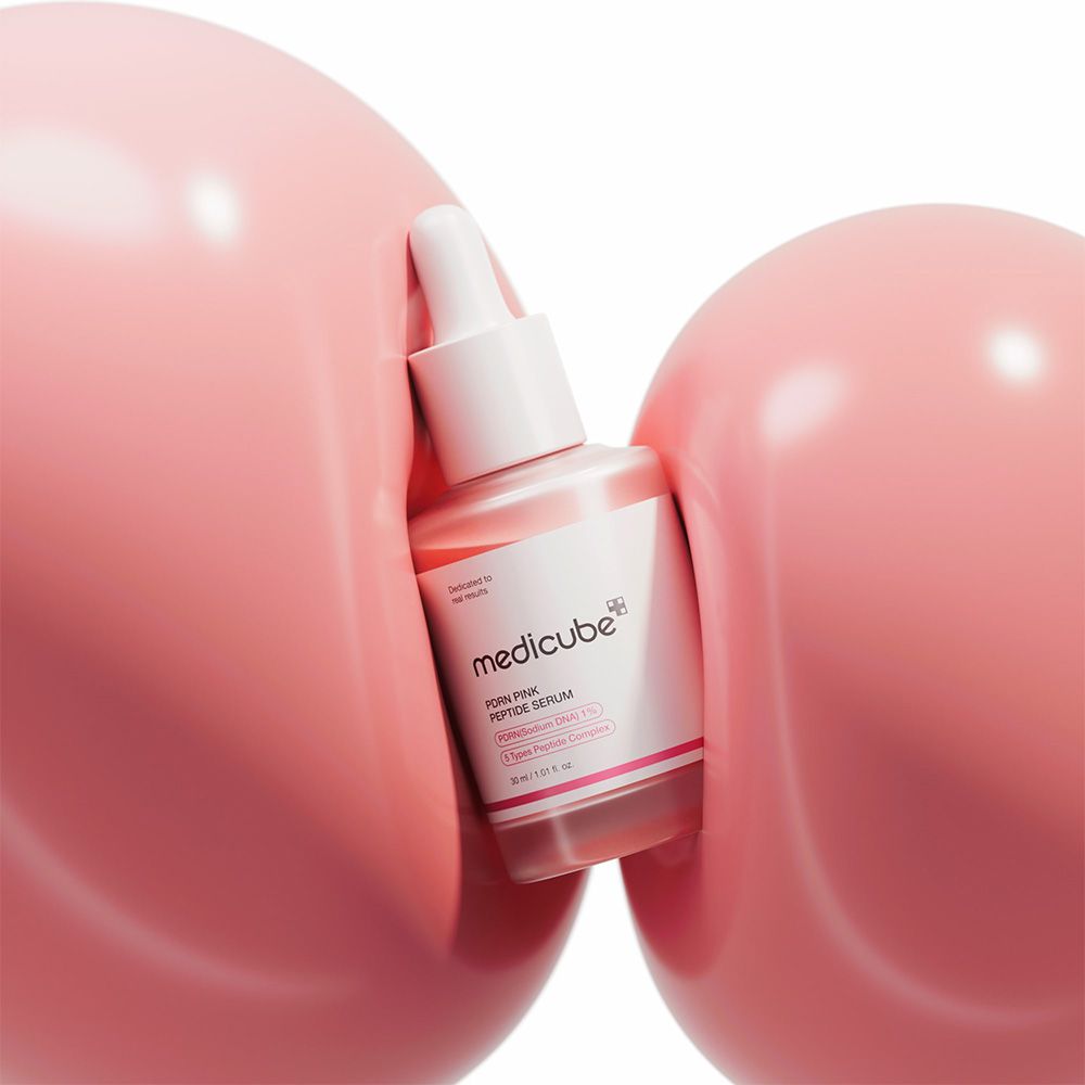 Flacone di Medicube PDRN Pink Peptide Serum tra due grandi sfere rosa.