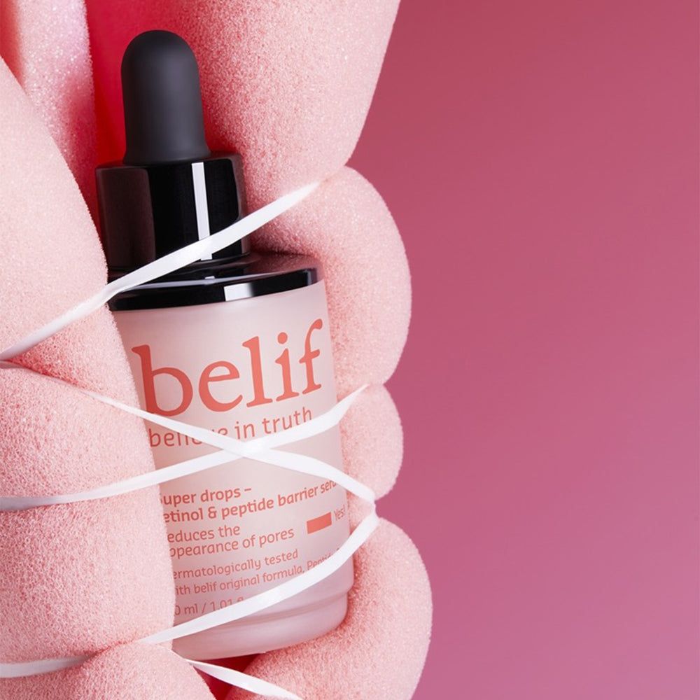 Mani tengono il flacone di siero Belif Super Drops, avvolto da nastro.