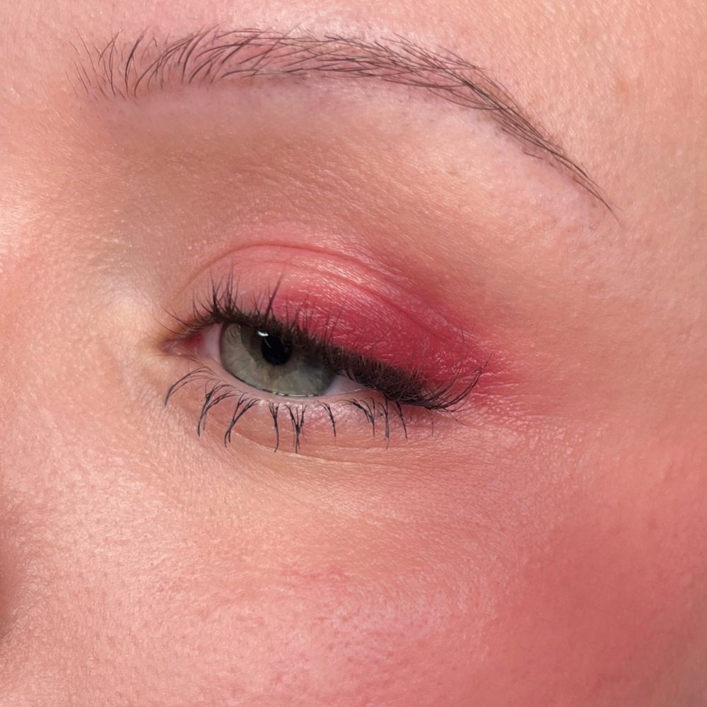 Primo piano di un occhio con ombretto rosso e mascara. Sfondo color carne.