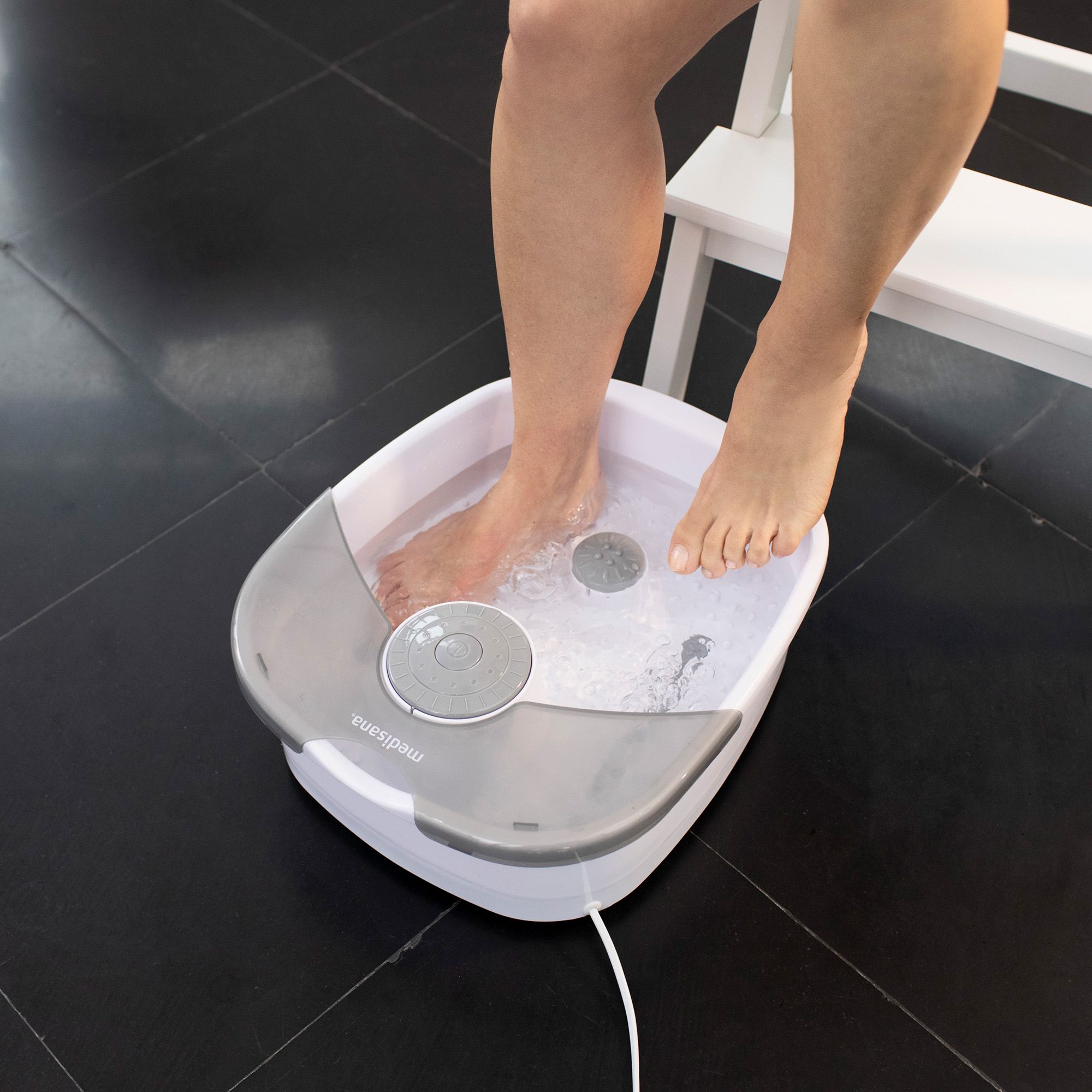 Idromassaggio per piedi in uso. Piedi nell'acqua. Dispositivo bianco e grigio con comandi. Cavo visibile.