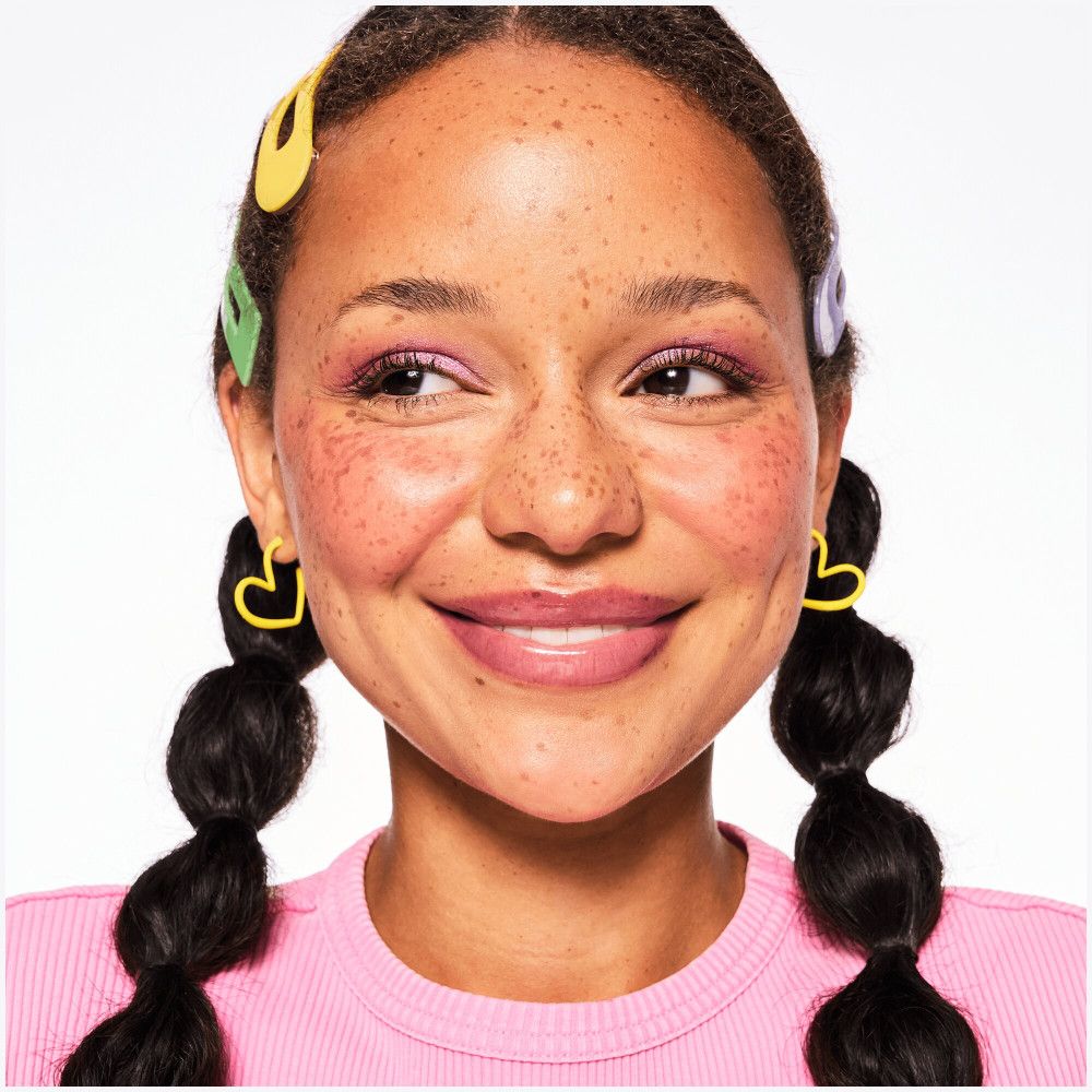 Ritratto di donna con lentiggini e labbra lucide. Orecchini a cuore gialli.