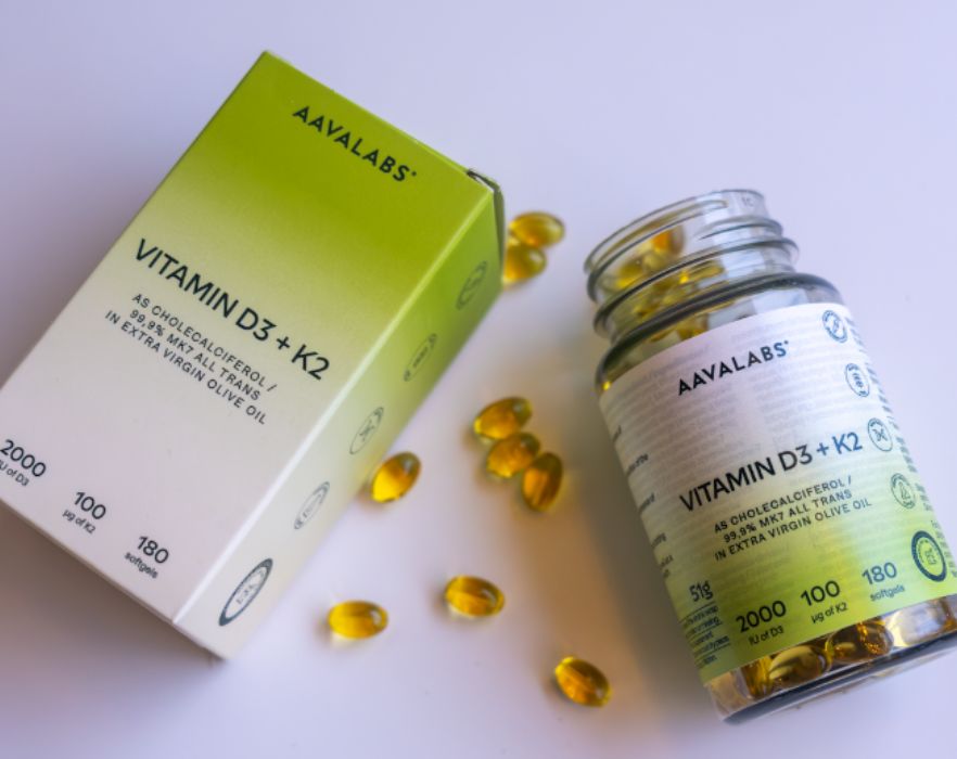 Aavalabs Vitamina D3+K2 Softgels accanto a una bottiglia aperta e una scatola, alcuni softgels sparsi.