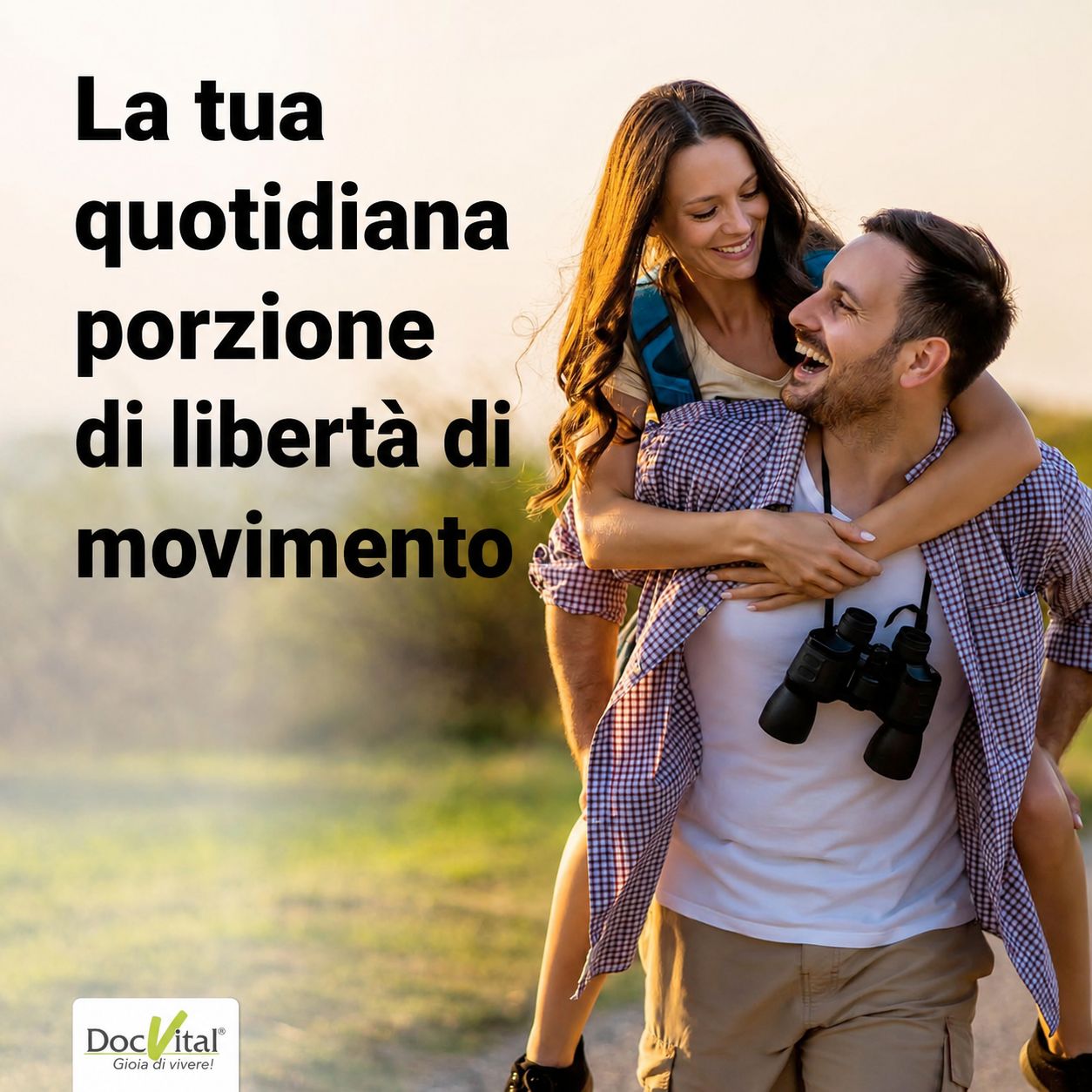 Un uomo porta una donna sulle spalle, entrambi sorridono. Indossano attrezzatura da trekking.