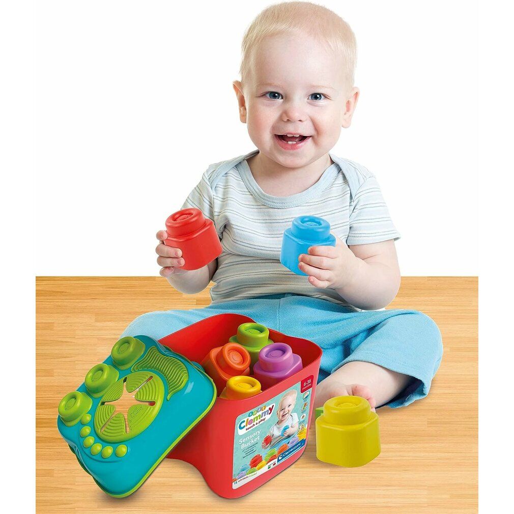 Bambino piccolo che gioca con Clementoni Sensory Bucket. Secchiello rosso, blocchi, coperchio con bottoni.