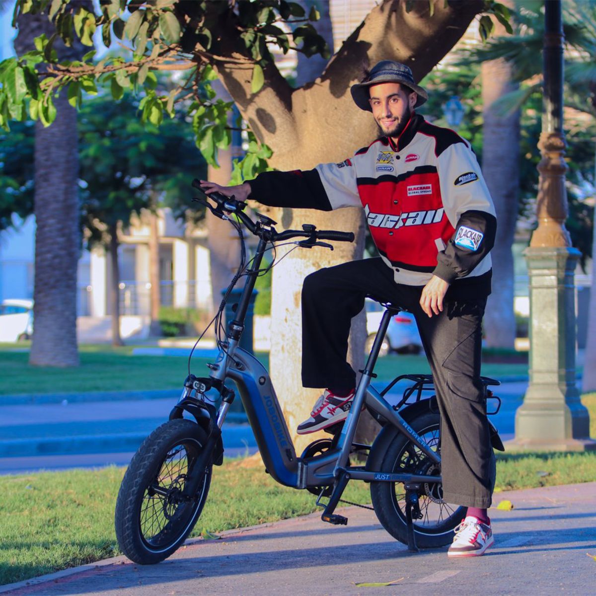 Uomo seduto su una e-bike JOBOBIKE Romer X blu. Indossa una giacca e un cappello. La bici è su un sentiero.