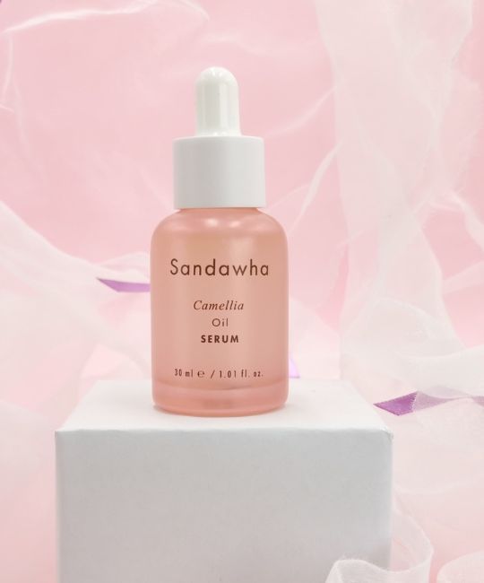Flacone di vetro rosa con contagocce bianco. Scritta: Sandawha, Camellia Oil Serum. Su piedistallo bianco.