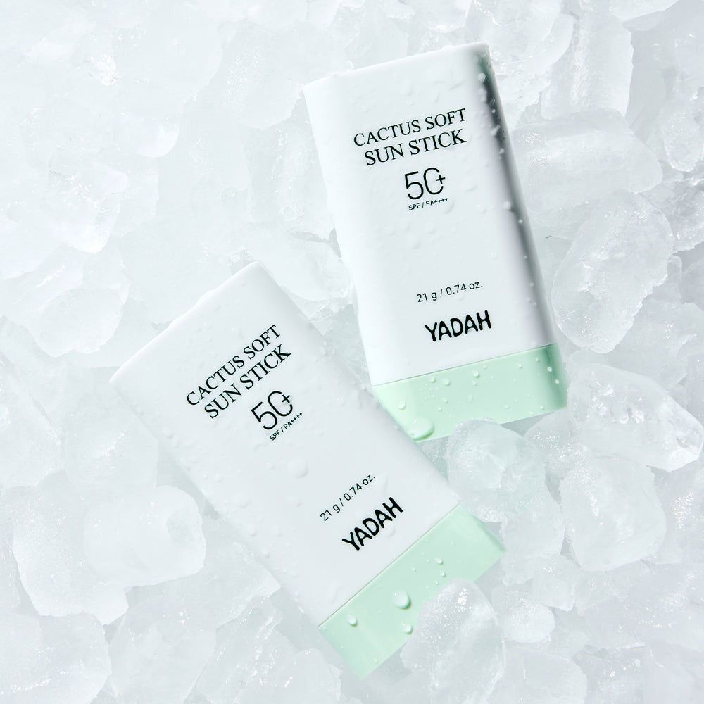 Due stick solari bianchi con estremità verdi su cubetti di ghiaccio. Scritto sopra: 'CACTUS SOFT SUN STICK 50'.