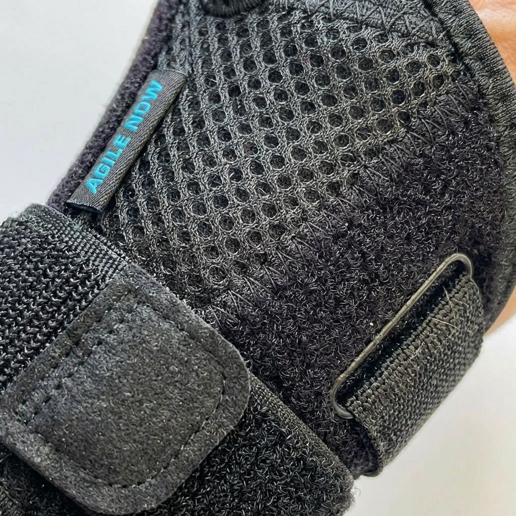 Primo piano di un tutore per pollice nero. Tessuto a rete, chiusure in velcro e logo AGILE NOW visibili.