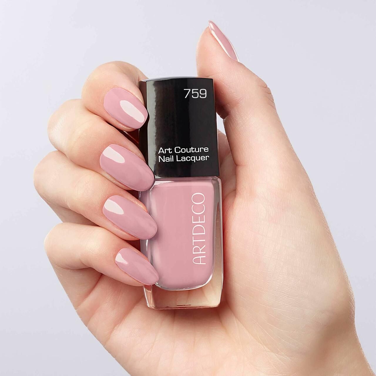 Mano che tiene un flacone di smalto. Smalto rosa sulle unghie. Tappo nero con scritta.