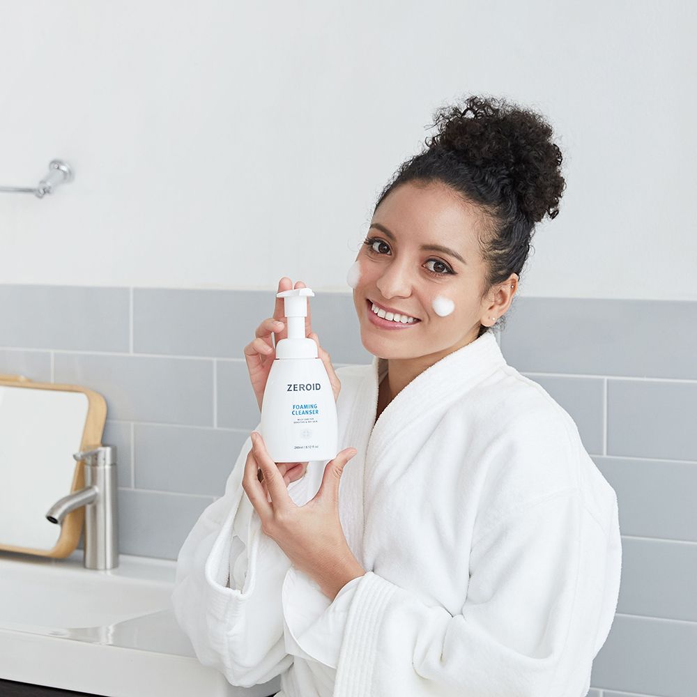 Donna che tiene in mano un flacone bianco ZEROID Foaming Cleanser. Testo: Foaming Cleanser, mild care for sensitive & dry skin. 240ml/8.12 fl oz.