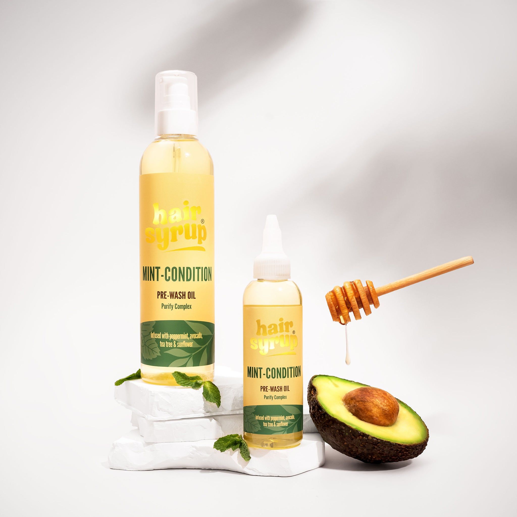 Due flaconi "Hair Syrup Mint Condition" vicino ad avocado e miele. Su pietre bianche.