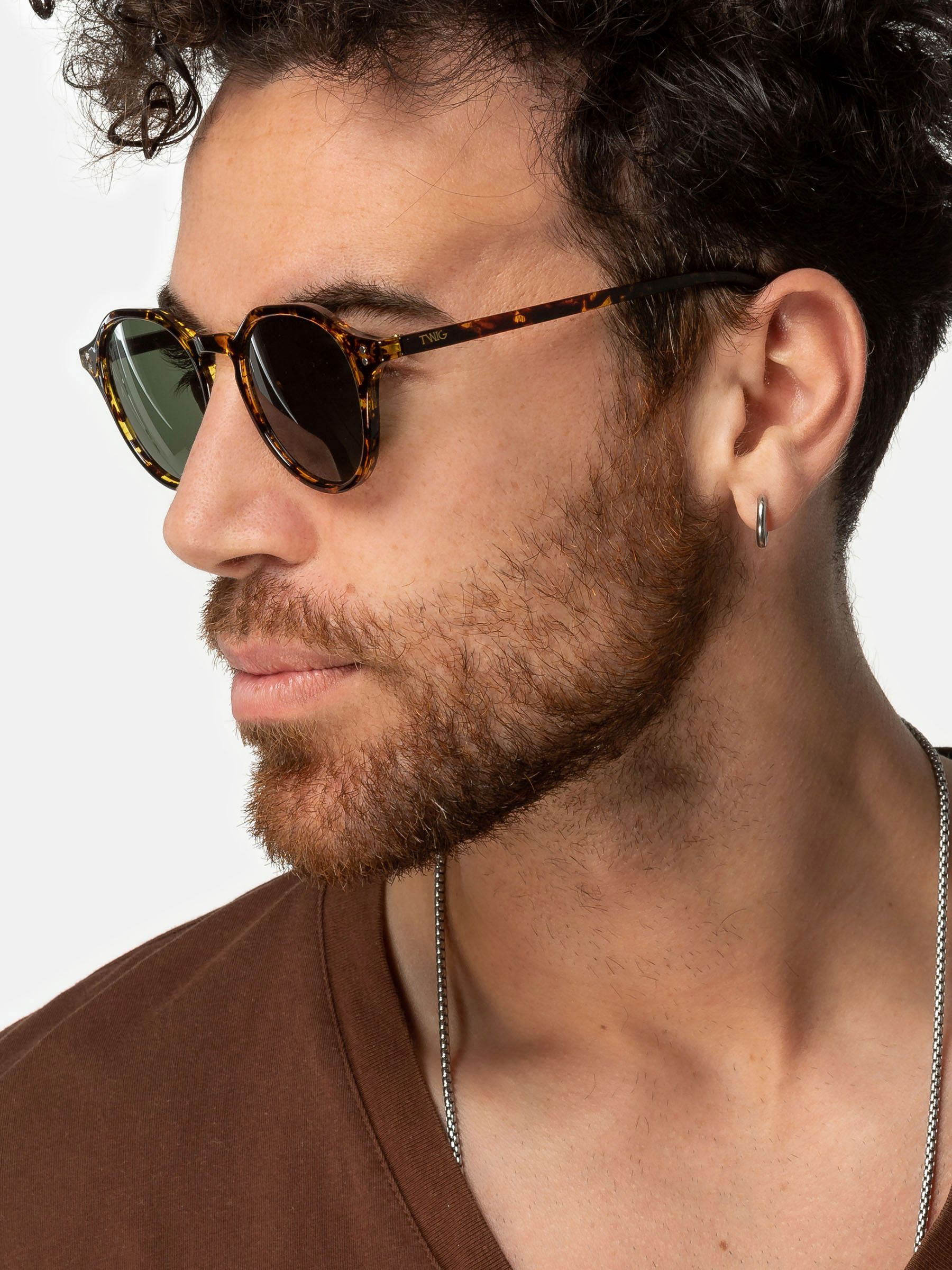 Uomo con occhiali da sole. Occhiali rotondi, motivo tartarugato marrone, lenti verdi. Vista laterale.