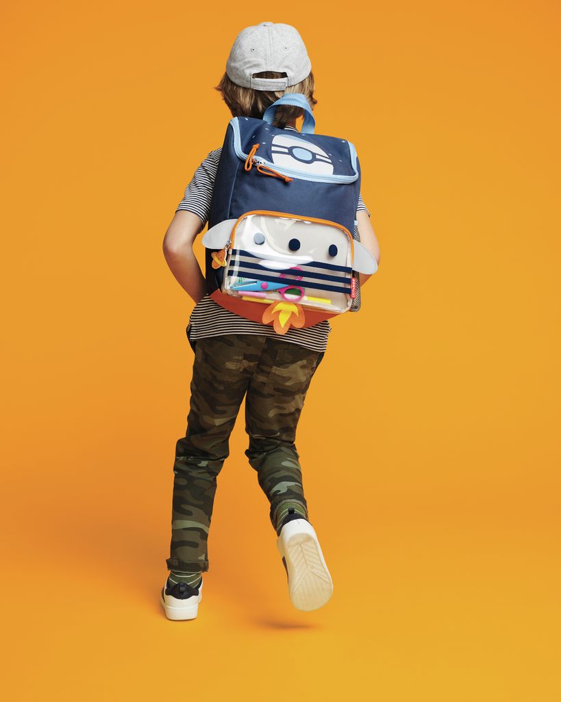 Bambino che indossa uno zaino blu scuro con un design a razzo. Lo zaino ha ali e una tasca frontale trasparente.