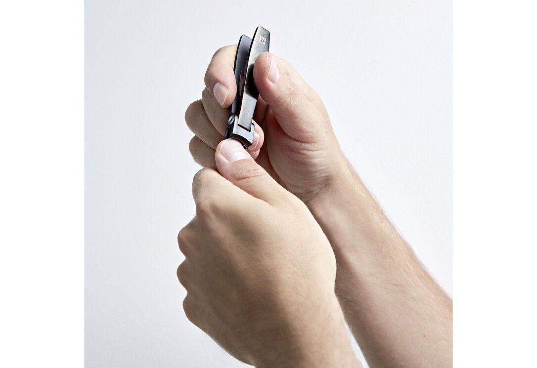 Mani che tengono un tagliaunghie nero. Il tagliaunghie viene aperto. Sfondo bianco.