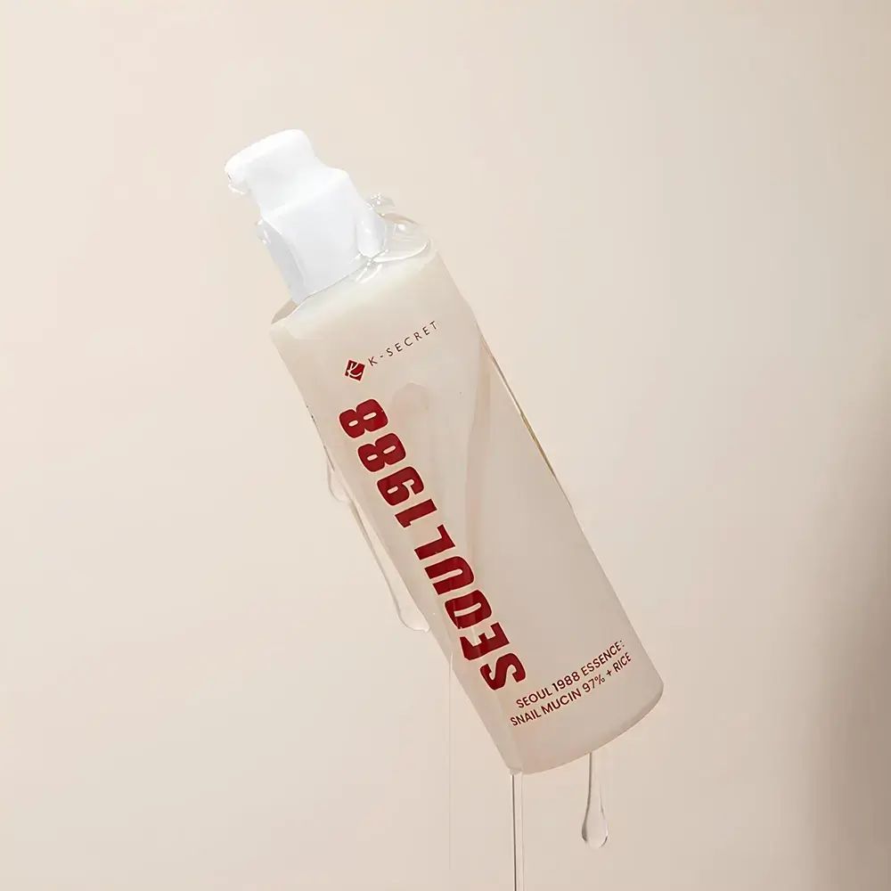 Flacone beige con erogatore bianco. Scritta rossa: SEOUL 1988. Nome del prodotto e ingredienti stampati. Liquido che cola.