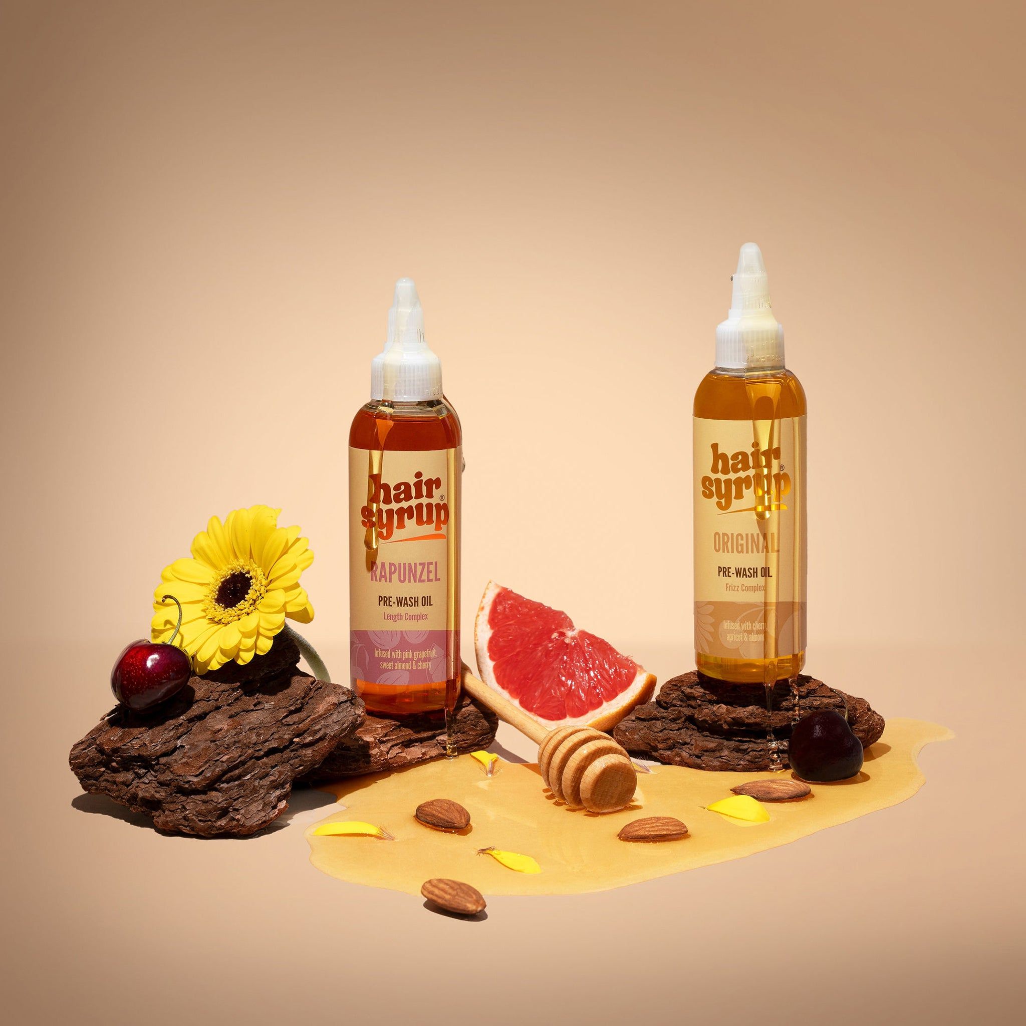 Due bottiglie di Hair Syrup, una con etichetta 'Original', l'altra 'Rapunzel'. Su pezzi di legno con pompelmo e miele.