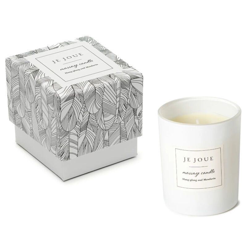 Candela bianca cilindrica e scatola con motivo a piume. Etichetta: Je Joue, massage candle. Ingredienti: Ylang Ylang e Mandarino.