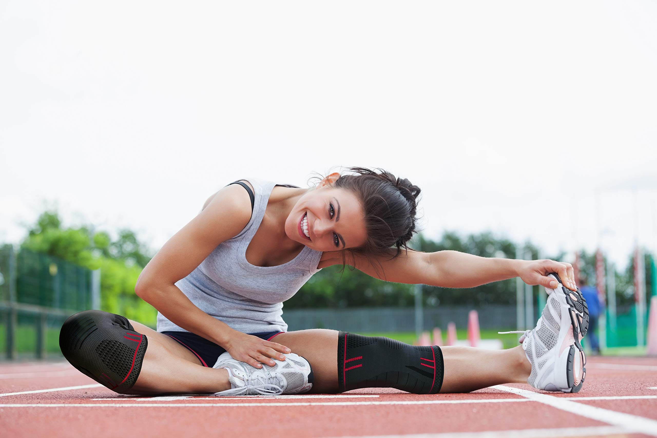 Donna che si allunga su una pista. Indossa ginocchiere. Materiale traspirante ed elastico.