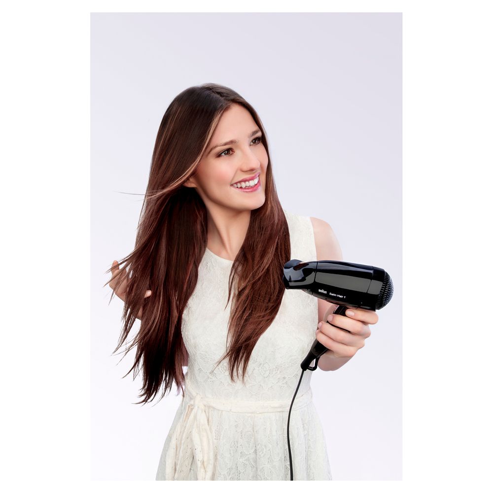 Donna con capelli lunghi tiene in mano un asciugacapelli nero Braun Satin Hair 1.