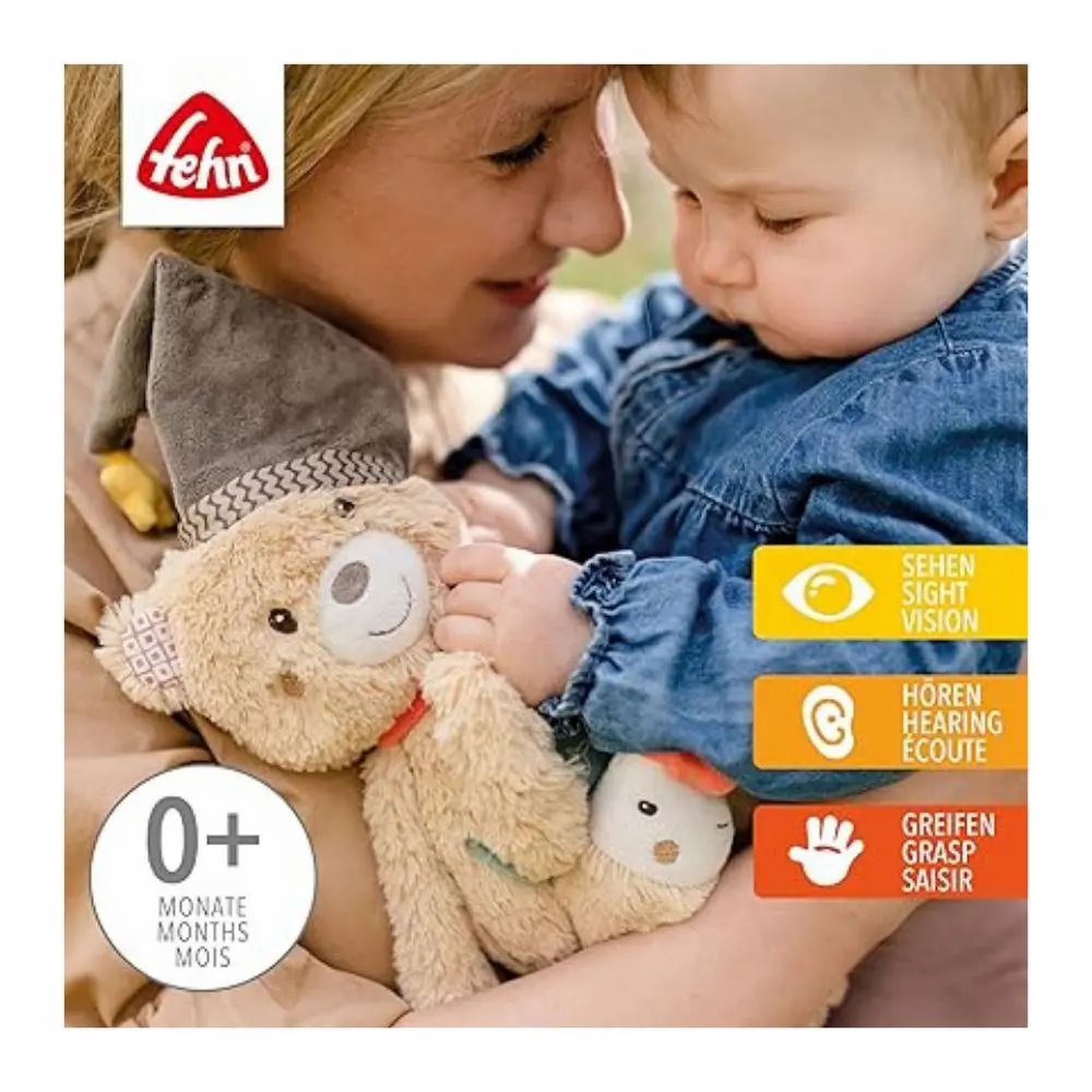 Bambino tiene peluche con cappello, sciarpa rossa, stella e pesce. Marchio: fehn. Con testo e simboli.