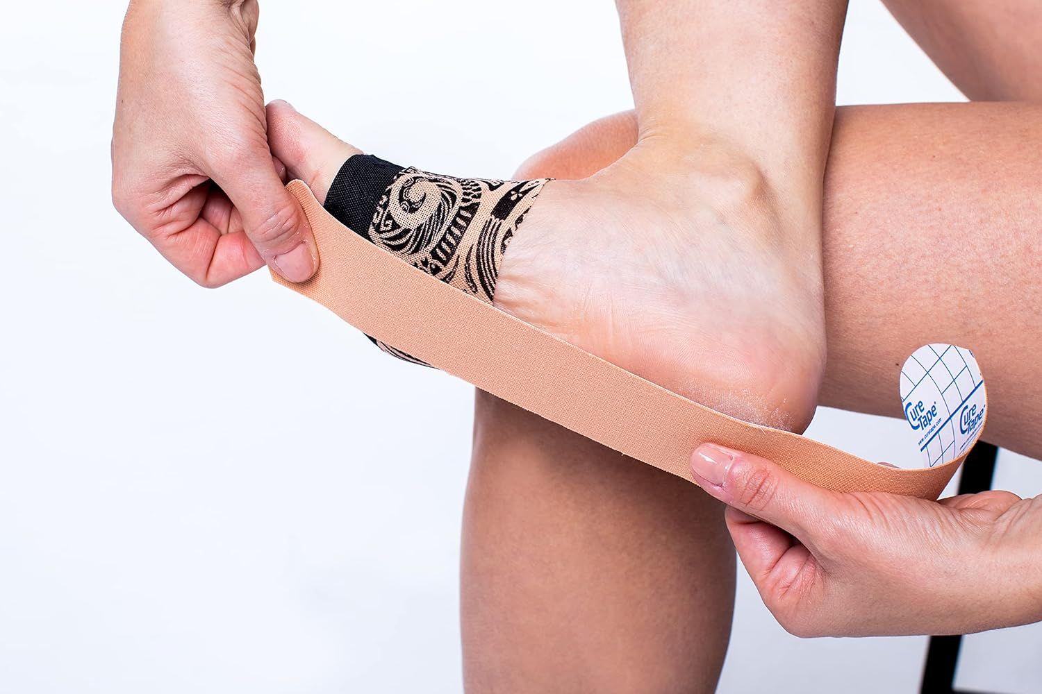 Persona applica nastro kinesiologico beige sul piede. Nastro applicato sul piede. Persona seduta. Tatuaggio sul piede.