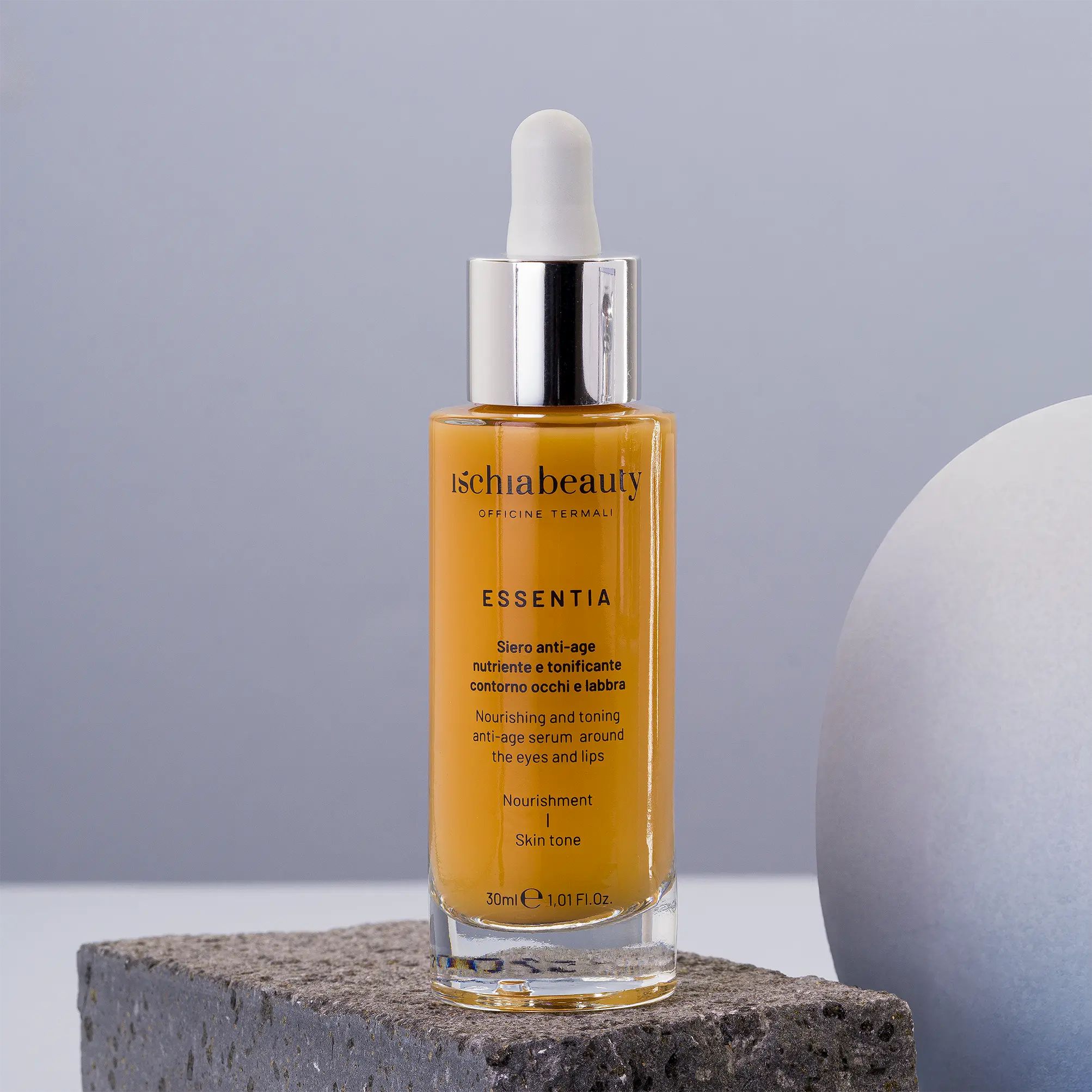 Flacone di siero ambrato con contagocce, su pietra. Scritta: Ischiabeauty, Essentia, Siero anti-age.