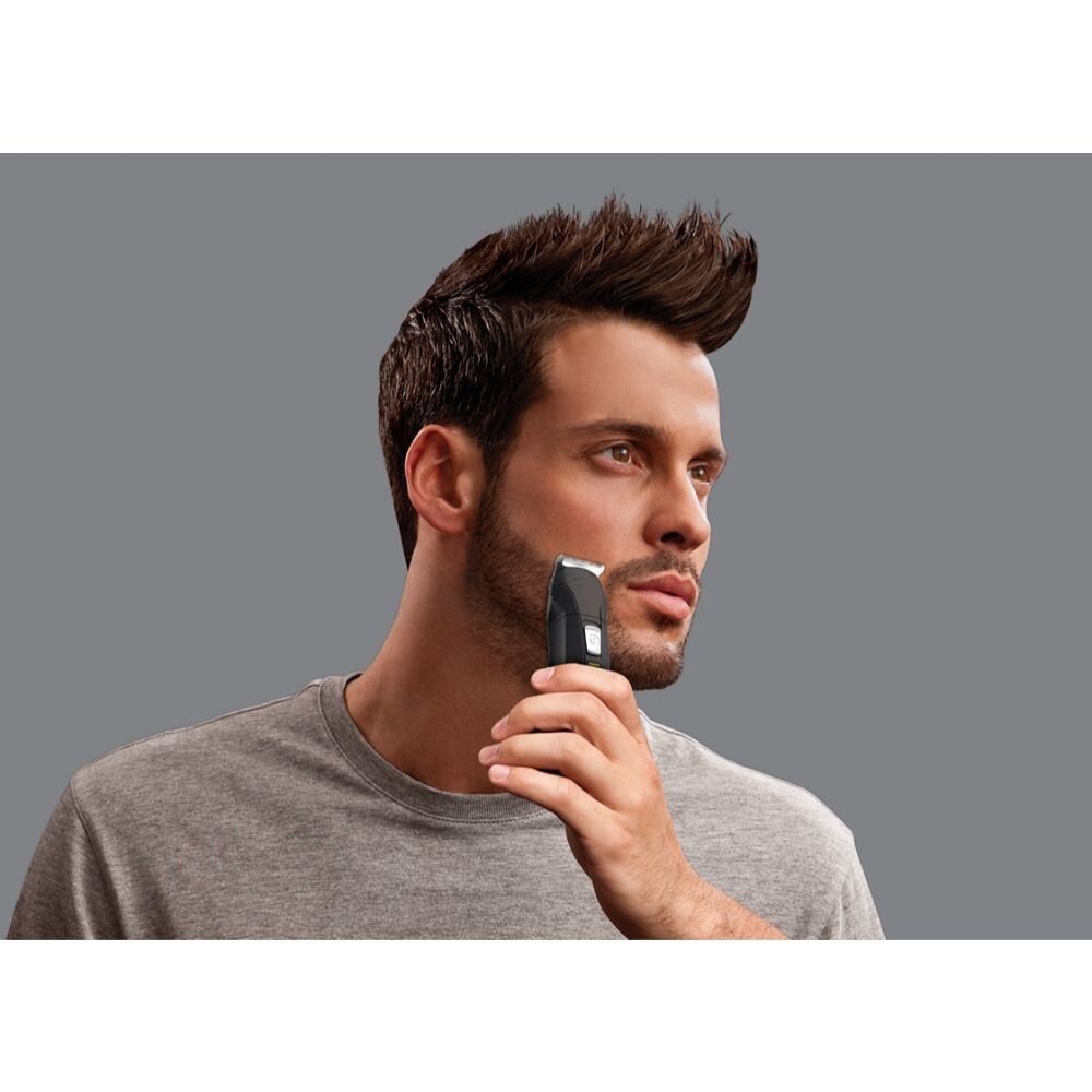Uomo che si rade la barba con un trimmer nero. Sfondo grigio. Trimmer in mano.