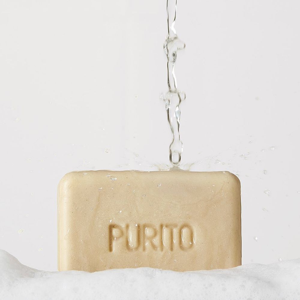 Sapone beige nella schiuma, con acqua versata sopra. Visibile la scritta "PURITO".